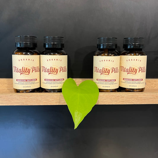 Four jars of Vitality Pills organic chicken liver capsules on a wooden shelf.